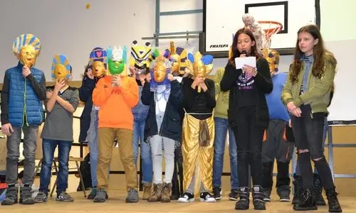 Schülerinnen und Schüler mit bunten Masken bei einer Aufführung in der Sporthalle