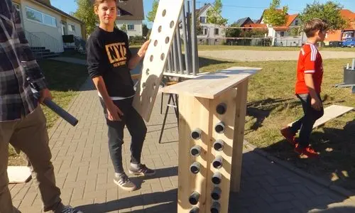Jugendliche im Freien neben einer selbst gebauten Holzkonstruktion mit eingesetzten Rohren
