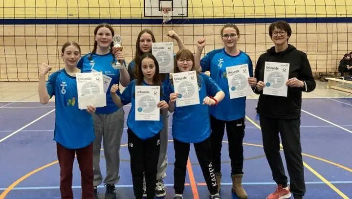 Volleyballerinnen in blauen Trikots mit Urkunden und Pokal und ihre Trainerin in der Sporthalle