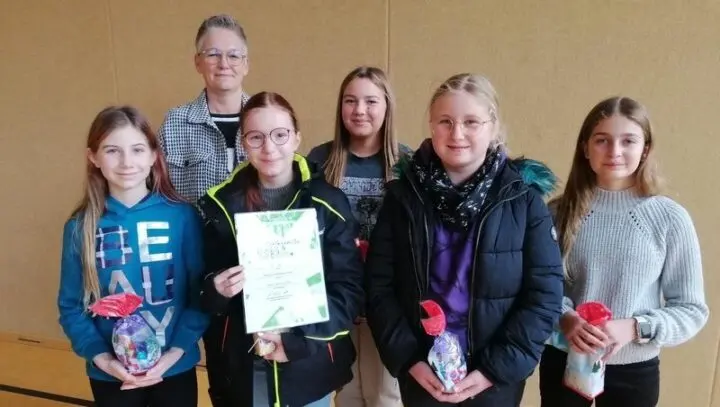 Fünf Schülerinnen mit Geschenktüten, eine hält eine Urkunde, dahinter eine Erwachsene