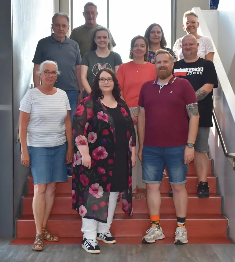 Zehn Erwachsene stehen für ein Gruppenfoto auf einer roten Treppe