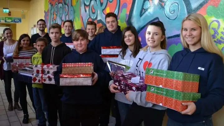 Schülerinnen und Schüler halten weihnachtlich verpackte Schuhkartons vor einer Graffitiwand