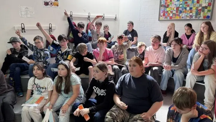 Schülerinnen und Schüler sitzen auf Stufen, einige melden sich