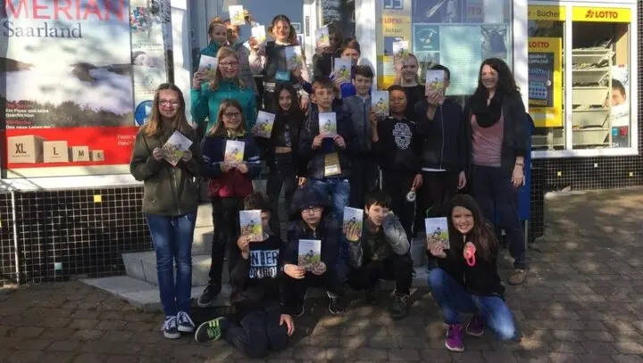 Schülerinnen und Schüler halten vor einem Schreibwarengeschäft ihre Buchgeschenke hoch