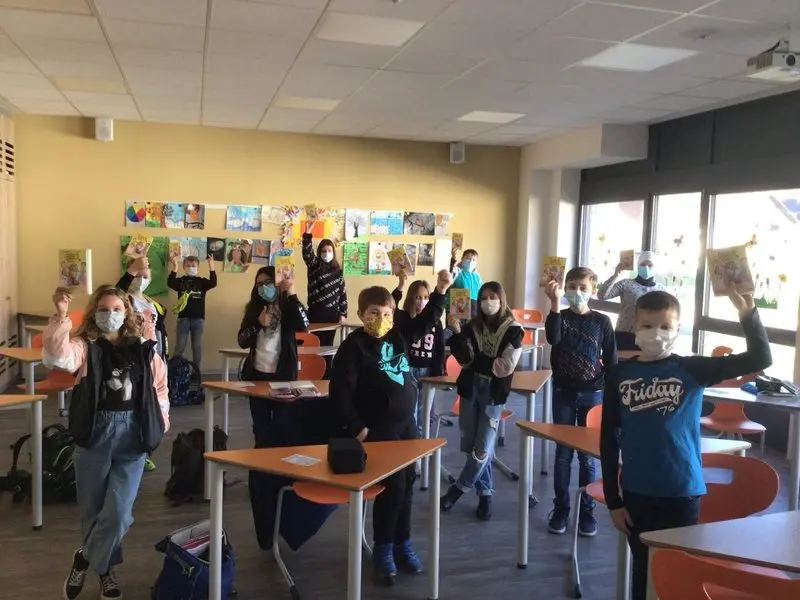 Schülerinnen und Schüler mit Masken stehen im Klassenraum und halten ihr Buchgeschenk hoch