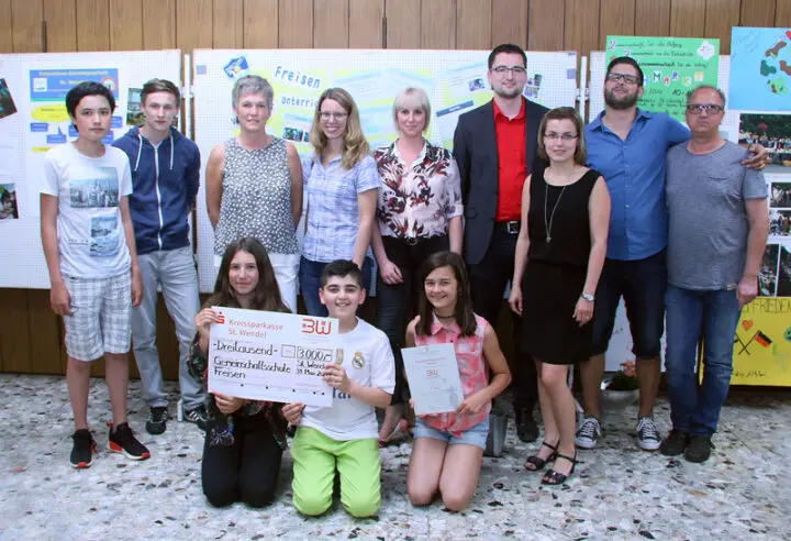 Gruppenfoto vor Projektwänden zum Vernetzten Unterricht, vorne Jugendliche mit Scheck über 3.000 Euro und Urkunde