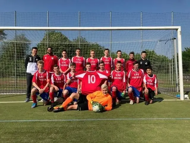 Fußballmannschaft in roten Trikots mit Betreuern vor einem Tor