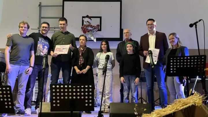 Gruppe auf einer Bühne mit Mikrofonen und Notenständern, zwei halten Urkunden