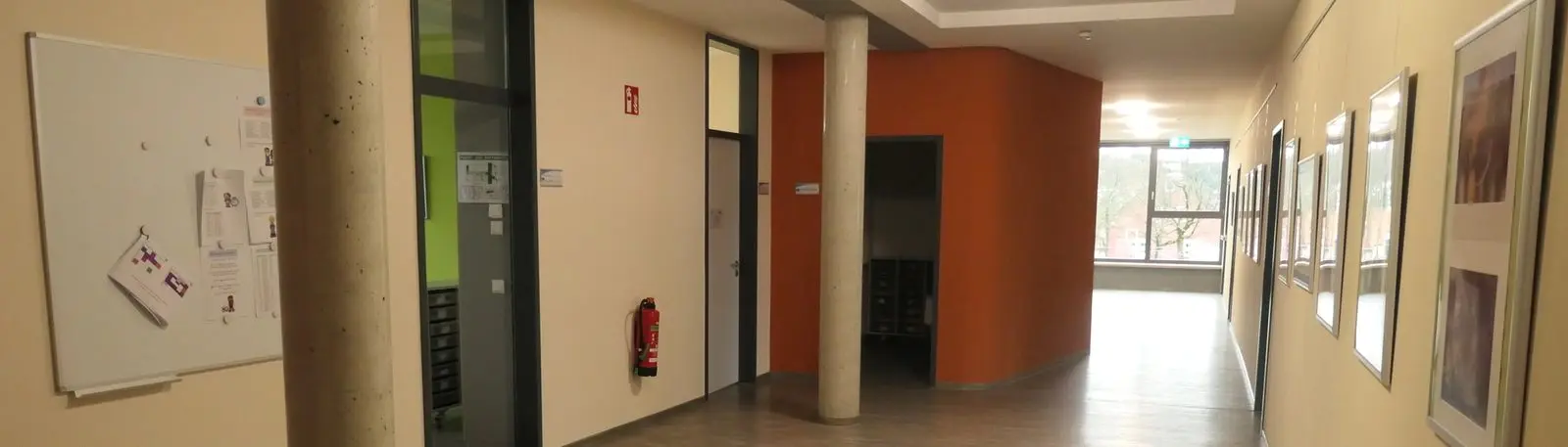 Heller Flur im Schulgebäude mit Säulen, orangefarbener Wand und gerahmten Bildern